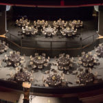 A view from the balcony, showing a gala seating arrangement of small tables on the floor level and stage of the Algonquin Commons Theatre.