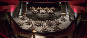 A view from the balcony, showing a gala seating arrangement of small tables on the floor level and stage of the Algonquin Commons Theatre.