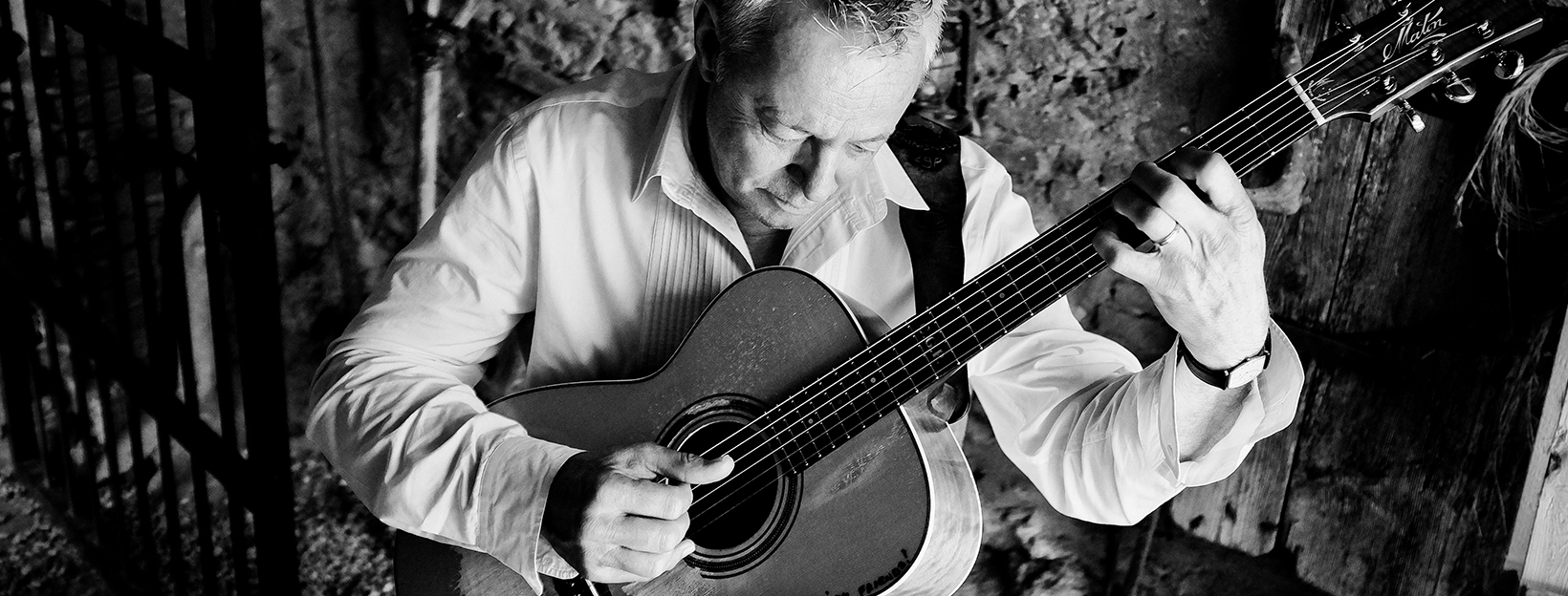 Tommy Emmanuel holding a guitar while wearing a white long sleeve dress shirt
